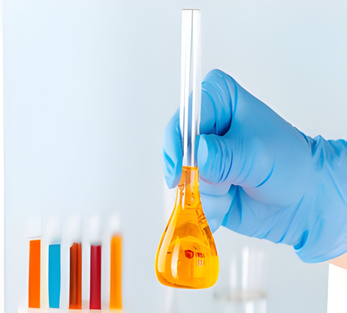 A gloved hand holds a glass flask containing orange liquid, set against a blurry row of colorful test tubes, conveying a scientific and analytical tone.